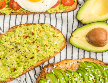 Three pieces of toast, one with mashed avocado, salt, and pepper, one with sliced avocado, feta, and honey, and one with mashed avocado, tomato, and a fried egg