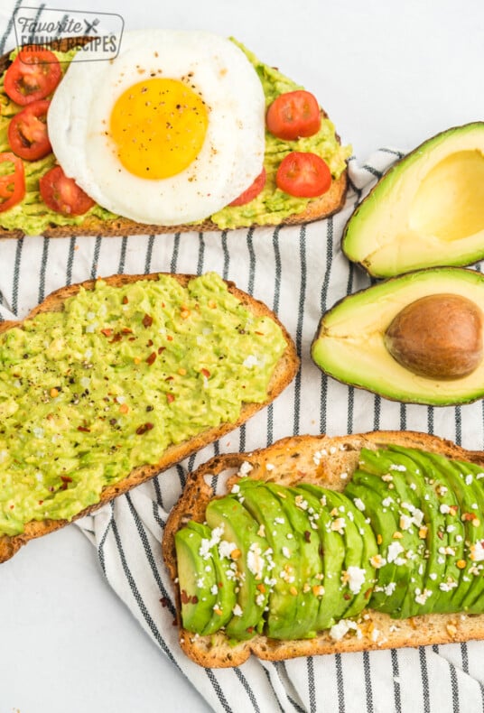 Three pieces of toast, one with mashed avocado, salt, and pepper, one with sliced avocado, feta, and honey, and one with mashed avocado, tomato, and a fried egg