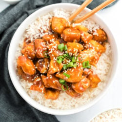 General Tso's Chicken in a bowl on a bed of rice topped with green onions and sesame seeds