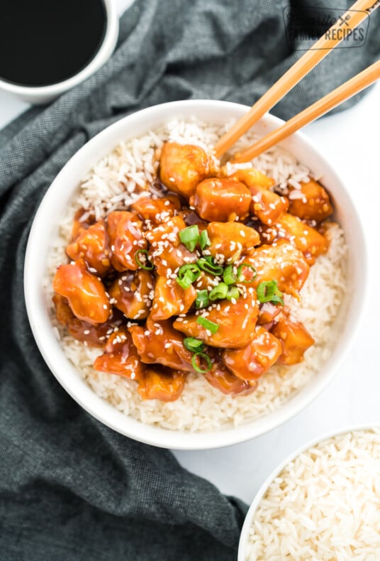 General Tso's Chicken in a bowl on a bed of rice topped with green onions and sesame seeds