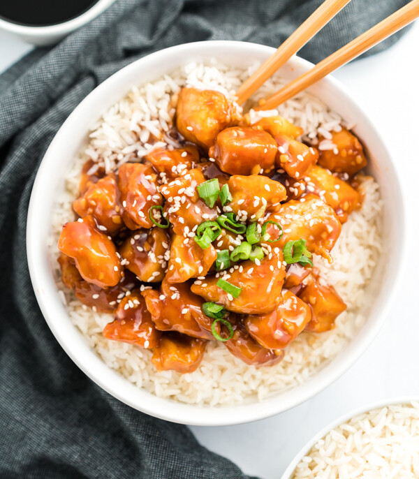 General Tso's Chicken in a bowl on a bed of rice topped with green onions and sesame seeds