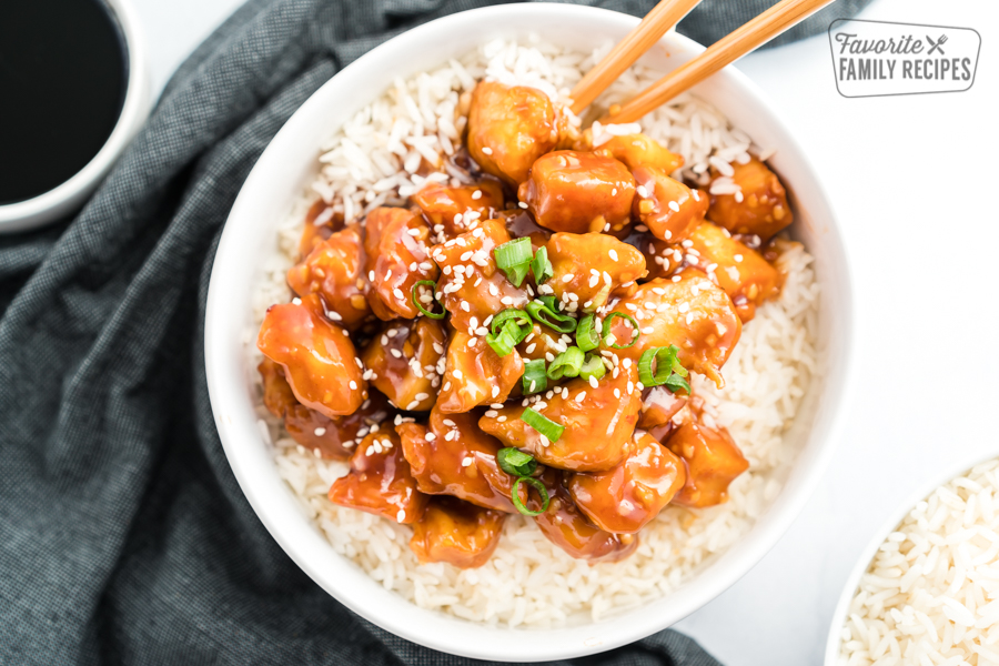 General Tso's Chicken in a bowl on a bed of rice topped with green onions and sesame seeds.