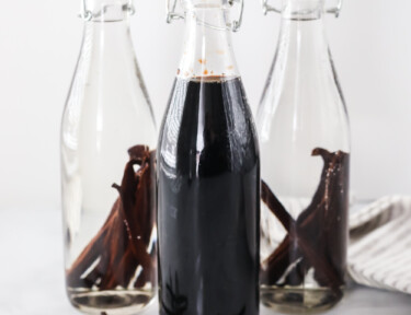 Two bottles of newly made vanilla extract with vanilla beans and one bottle of mature vanilla extract