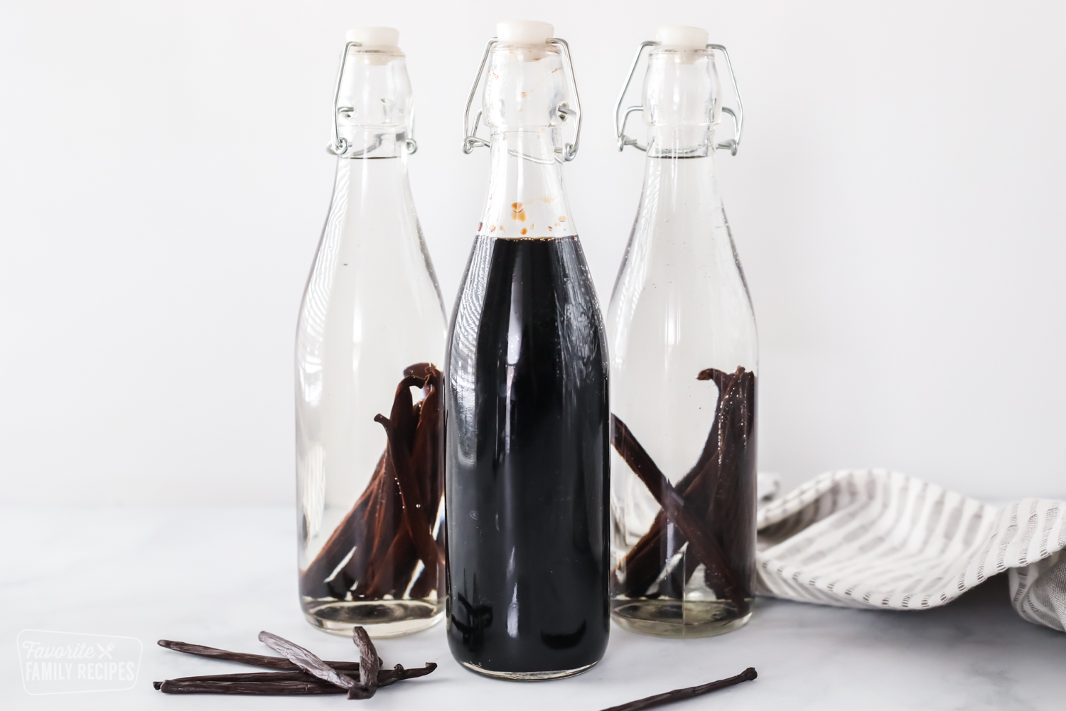 Two bottles of newly made vanilla extract and one bottle of mature vanilla extract with vanilla beans.