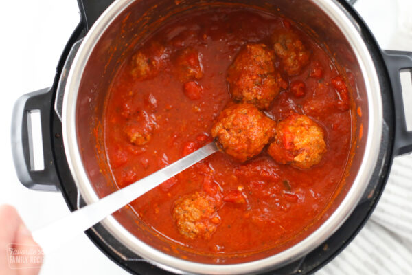 Meatballs in an Instant Pot being served with a serving spoon.