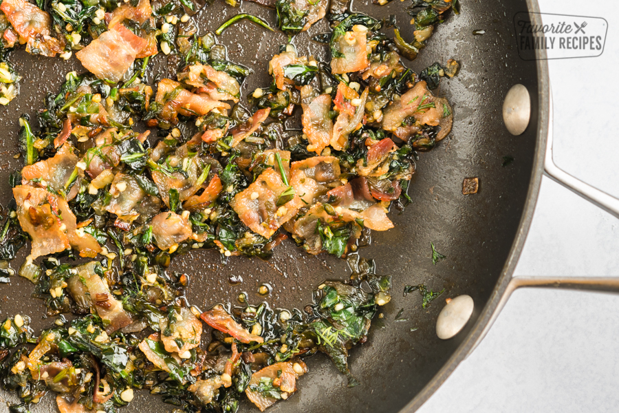 Spinach, bacon, garlic, and oil cooking in a skillet
