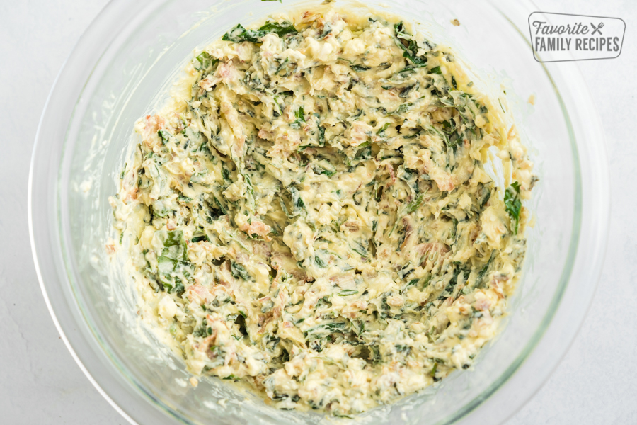 Spinach, bacon, feta, cream cheese, garlic, and spices mixed together in a glass bowl