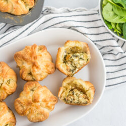 Spinach Puffs on a white plate with one cut open to reveal the cheese and spinach filling