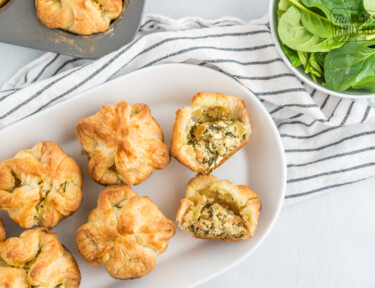 Spinach Puffs on a white plate with one cut open to reveal the cheese and spinach filling