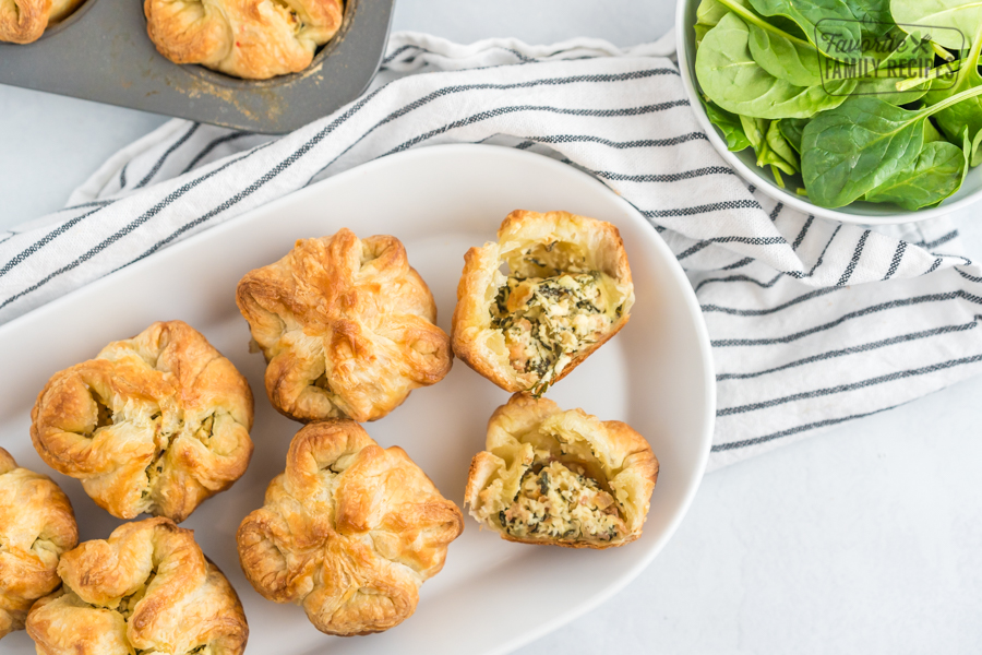 Spinach Puffs on a white plate with one cut open to reveal the cheese and spinach filling.