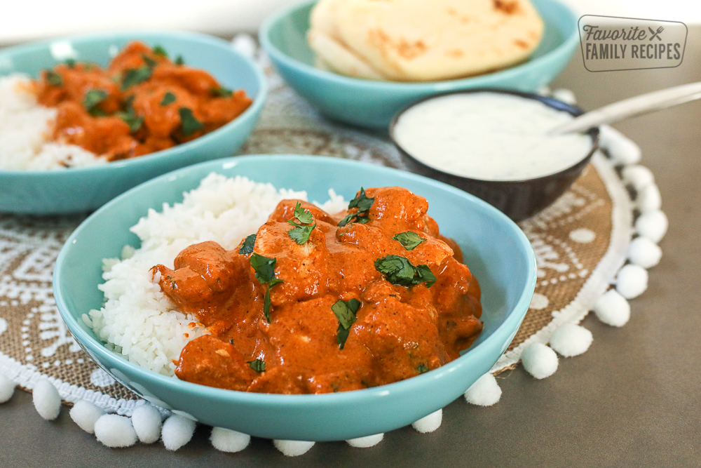 A blue bowl filled with Chicken Tikka Masala and rice. Naan bread and yogurt on the side.