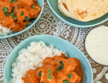 Chicken Tikka Masala in a bowl with rice and a side of yogurt dip and naan bread