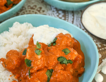 Chicken Tikka Masala in a bowl with rice and cucumber yogurt dip