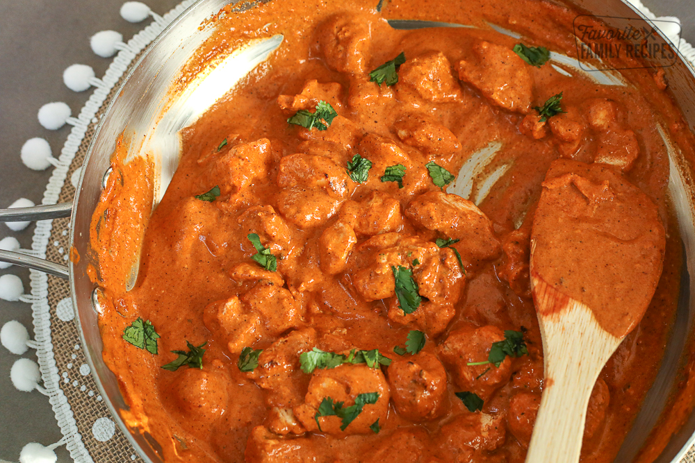 Chicken Tikka Masala cooking in a large skillet and stirred with a wooden spoon.