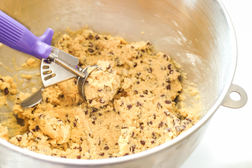 Chocolate chip cookie dough in a mixing bowl with a purple cookie scoop.