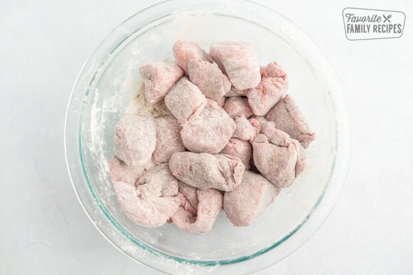 A glass bowl full of beef stew pieces coated in flour