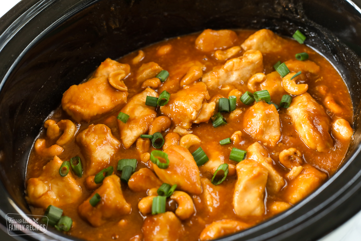 Close up of cashew chicken in a Crock Pot with green onion and cashews