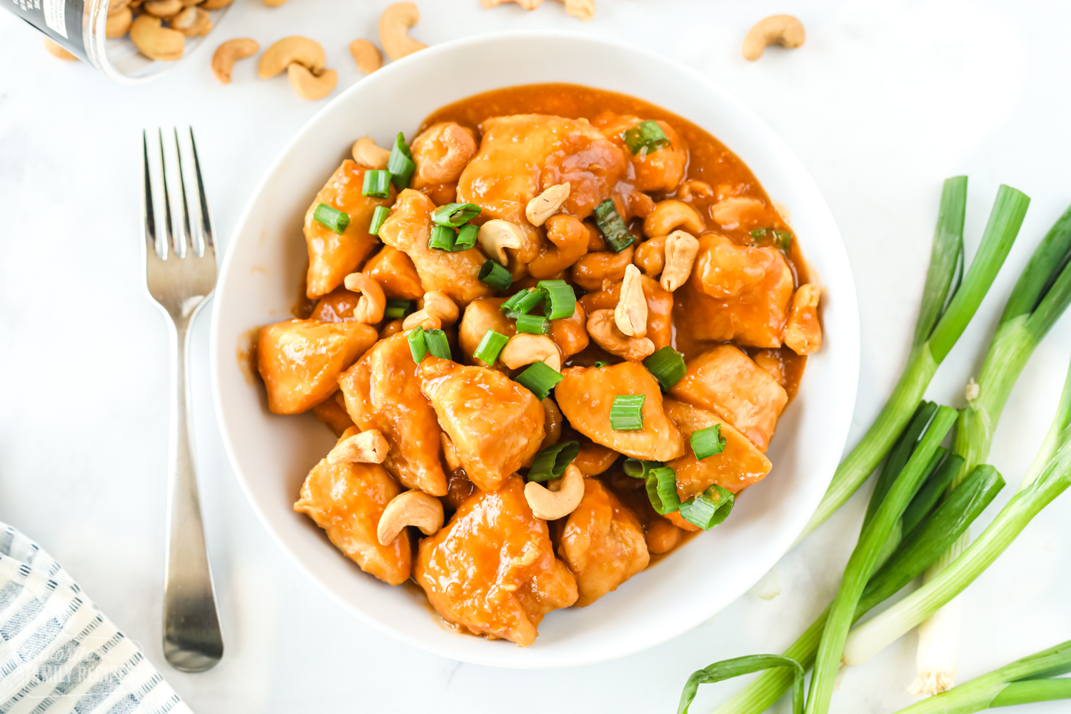 A bowl of cashew chicken with sauce, cashews, and green onion