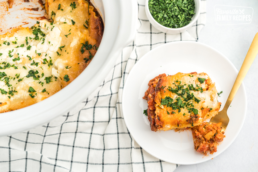 A slice of crock pot lasagna on a white plate with a gold fork