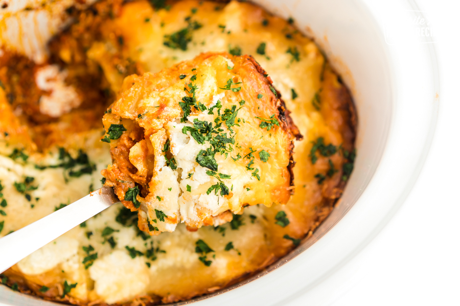 A scoop of crock pot lasagna being taken out of a slow cooker