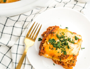 A slice of crock pot lasagna on a white plate with a gold fork