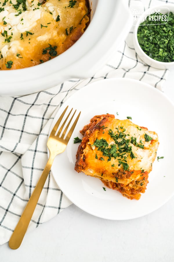A slice of crock pot lasagna on a white plate with a gold fork