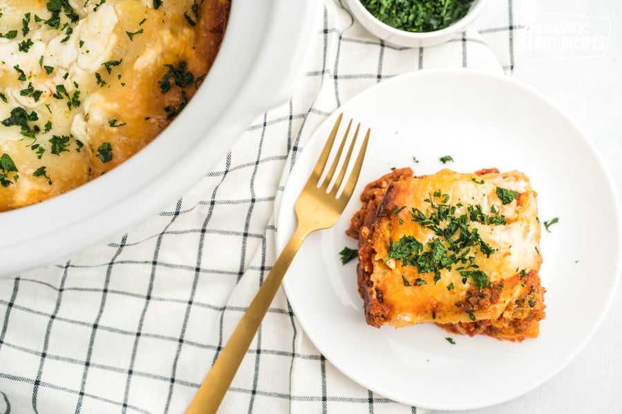 A slice of crock pot lasagna on a white plate with a gold fork.