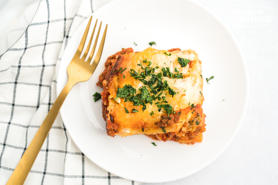 A slice of crock pot lasagna on a white plate with a gold fork.