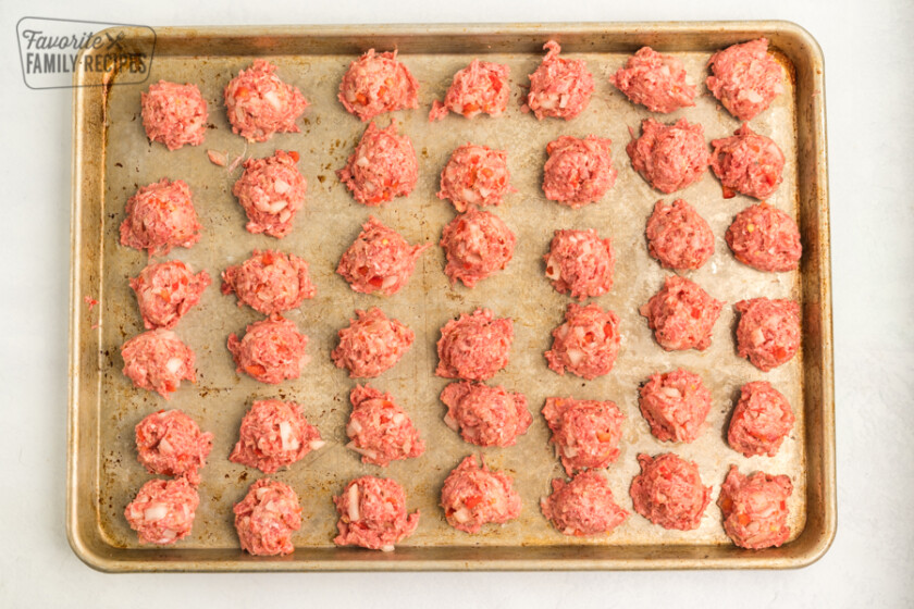 Uncooked meatballs lined up on a baking sheet
