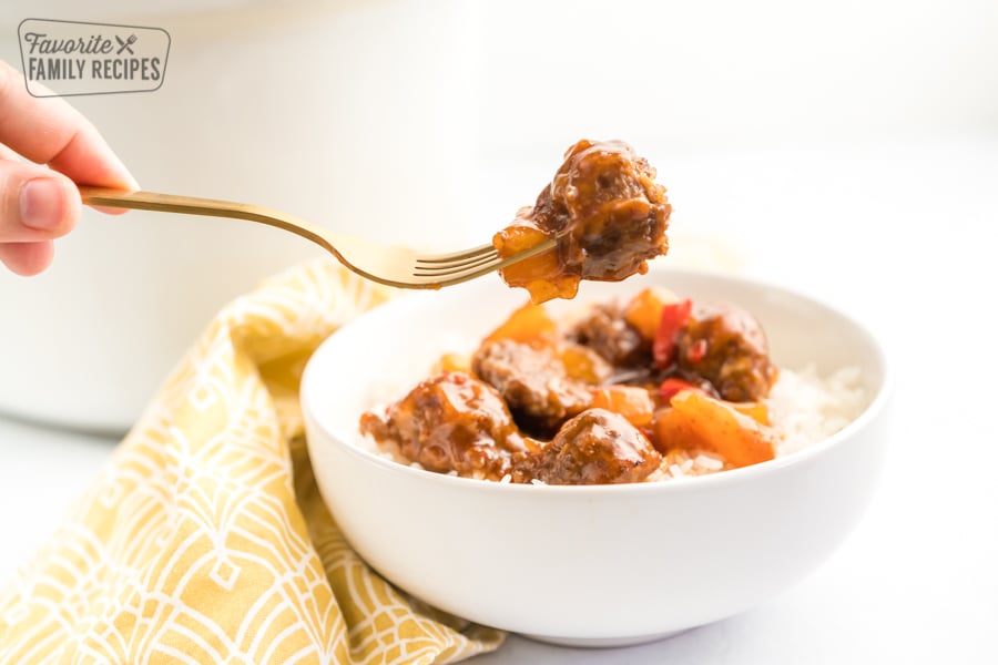 A meatball on a fork above a bowl of rice and meatballs