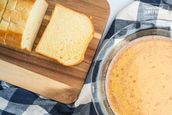 Egg batter for making French Toast in a glass pie dish next to a loaf of sliced brioche bread.