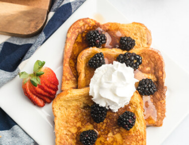 A plate of French toast slices topped with blackberries, syrup and whipped cream