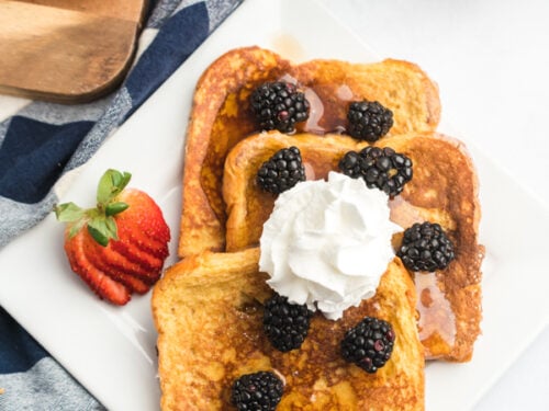 A plate of French toast slices topped with blackberries, syrup and whipped cream