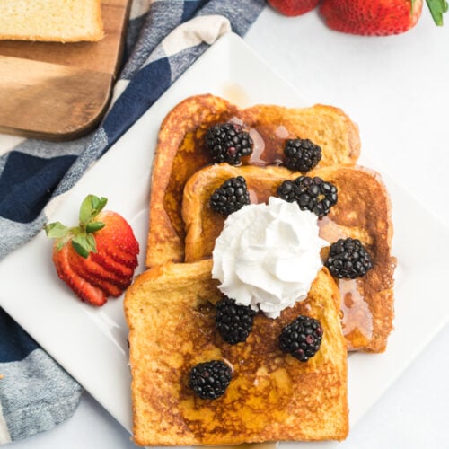 A plate of French toast slices topped with blackberries, syrup and whipped cream