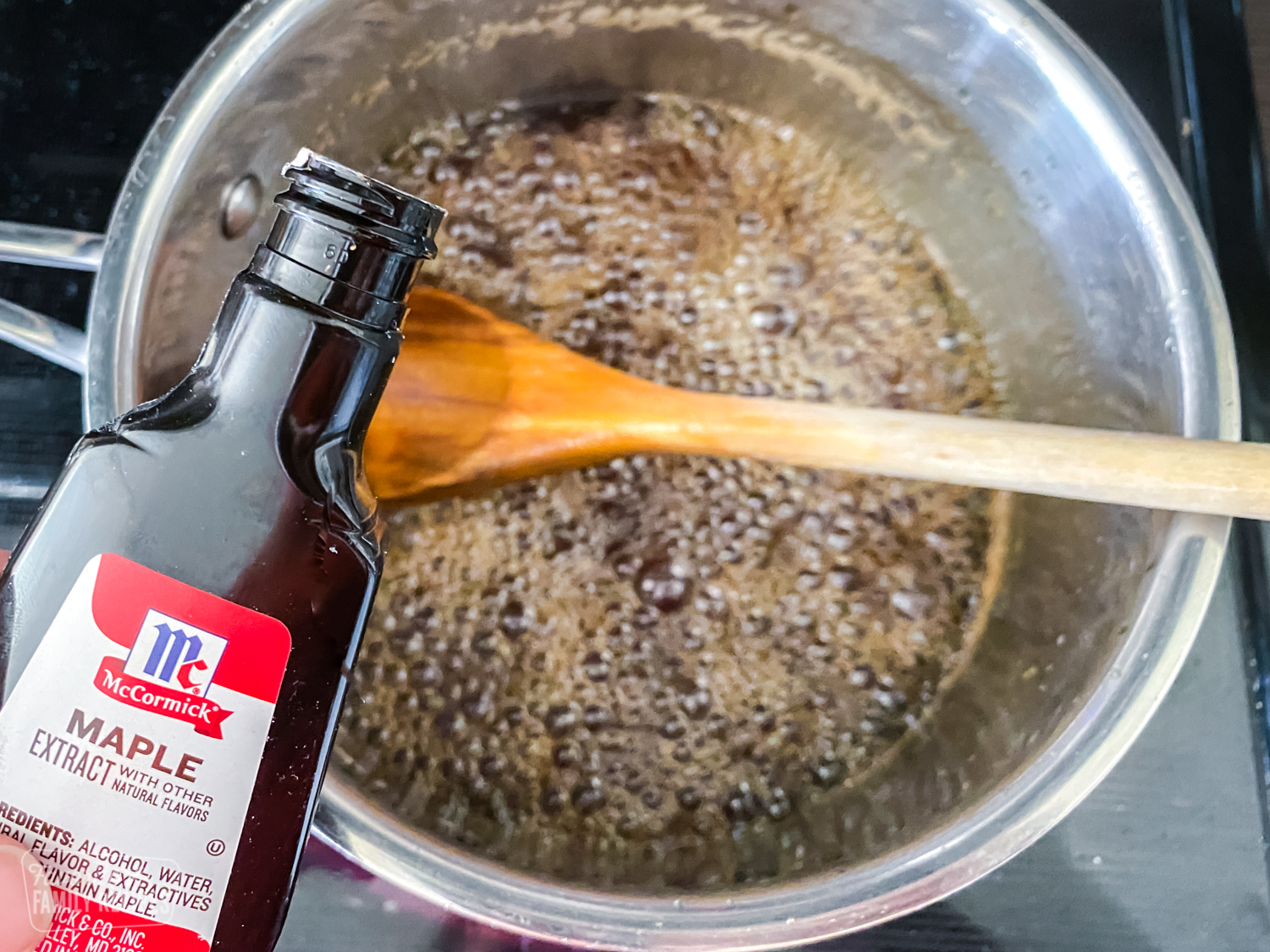 Maple extract being poured into a sauce pan with homemade maple syrup