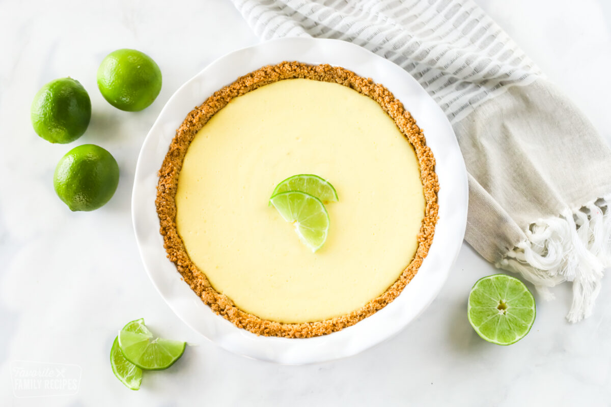 A top view of a fresh key lime pie with lime wedges and whole limes