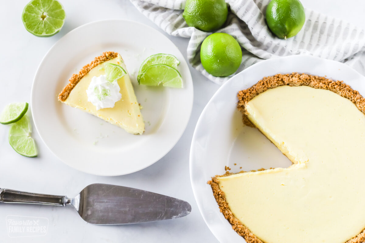 A whole key lime pie made with graham cracker crust and a slice taken out of it with limes as garnishes