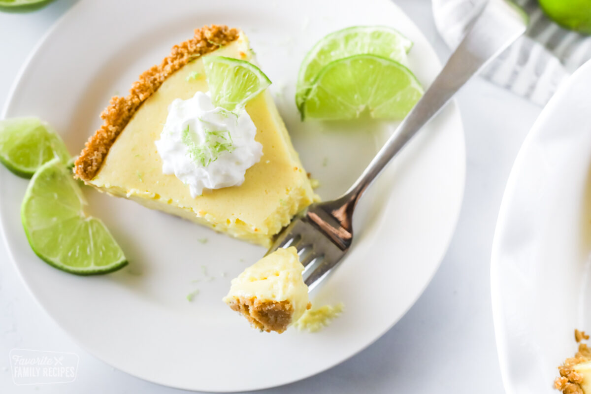 A slice of key lime pie with a graham cracker crust and a bite on a fork