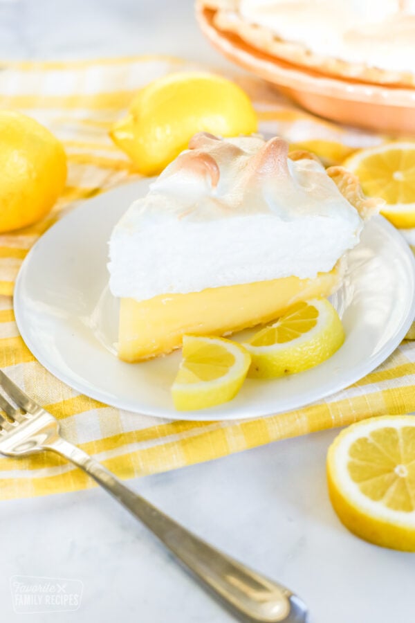 A slice of lemon meringue pie on a plate garnished with lemon wedges