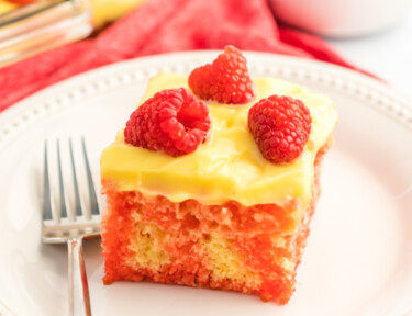 Raspberry Lemon Jello Poke Cake topped with lemon pudding frosting and fresh raspberries