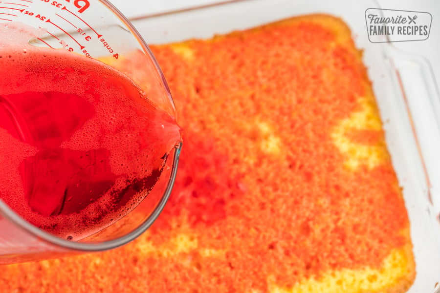 Pouring raspberry jello mix over a cake