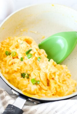 Close up of scrambled eggs in a pan with a green spatula underneath ready to lift the eggs from the pan.