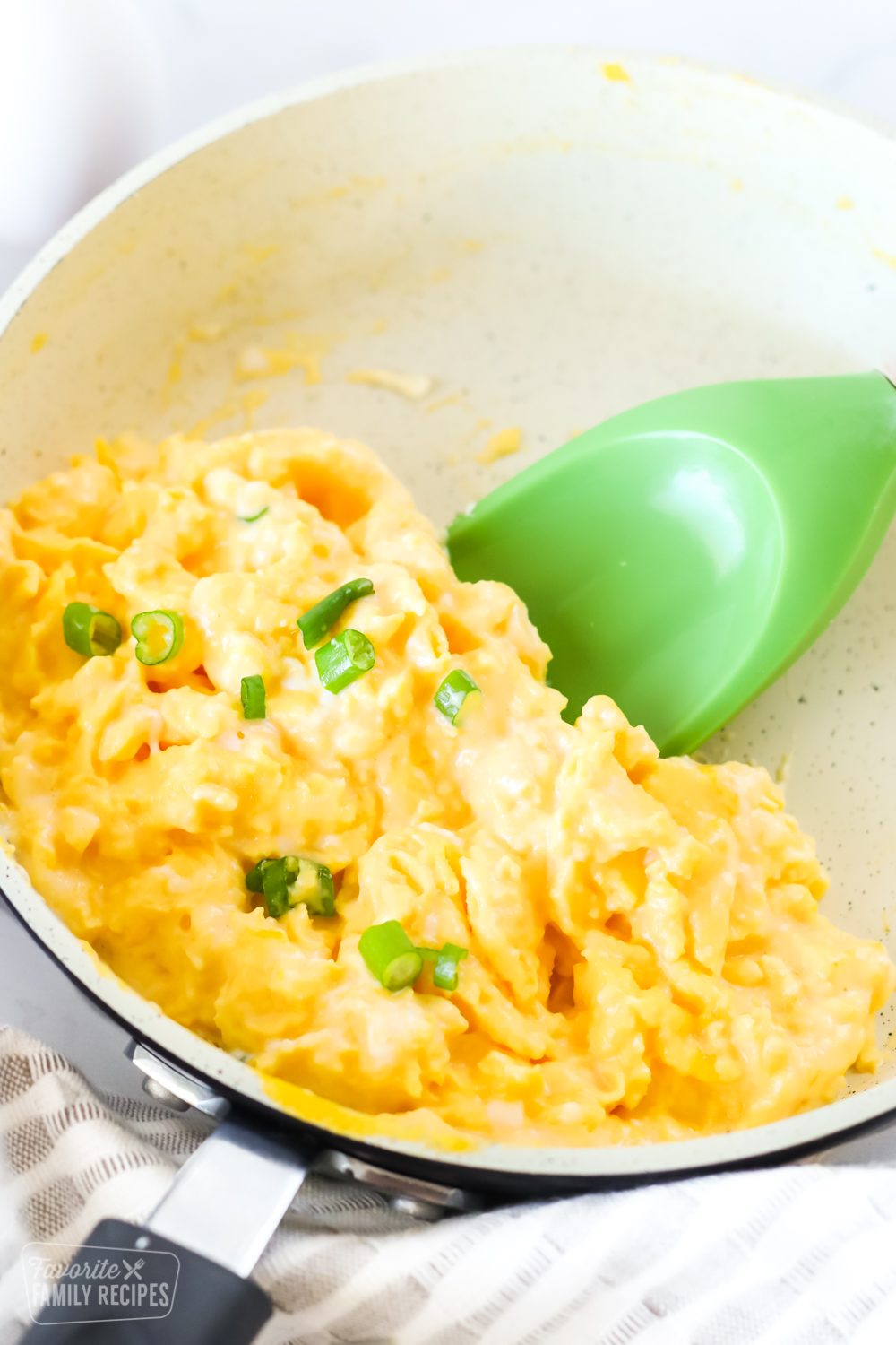 Close up of scrambled eggs in a pan with a green spatula underneath ready to lift the eggs from the pan.