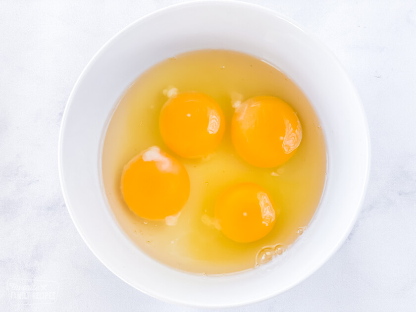 Four egg yolks sitting in eggs whites in a small bowl.