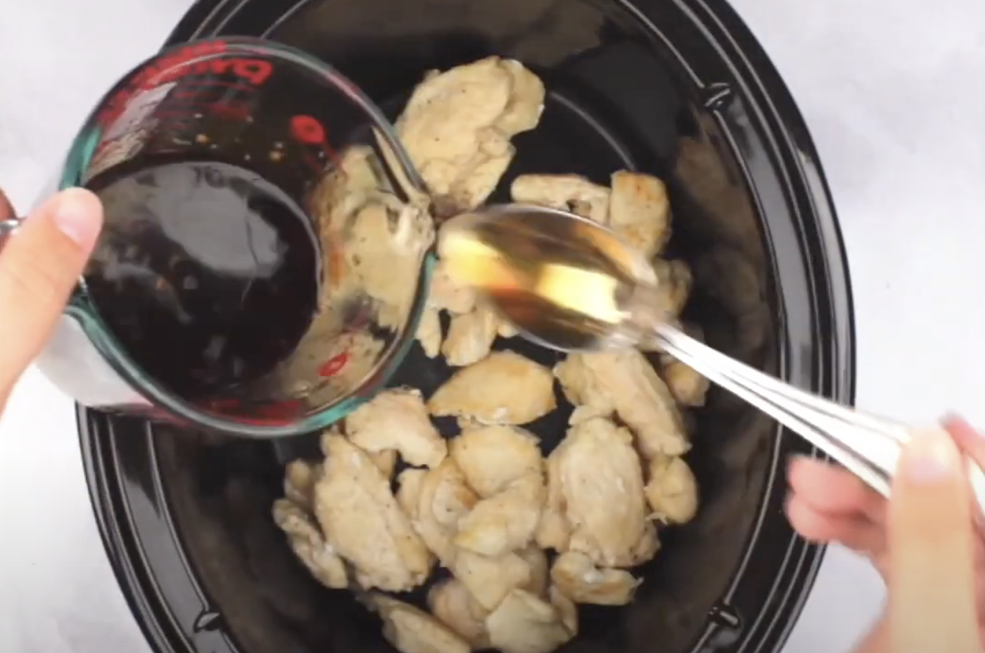 Chicken in a Crock Pot with sauce being poured over the top to make cashew chicken