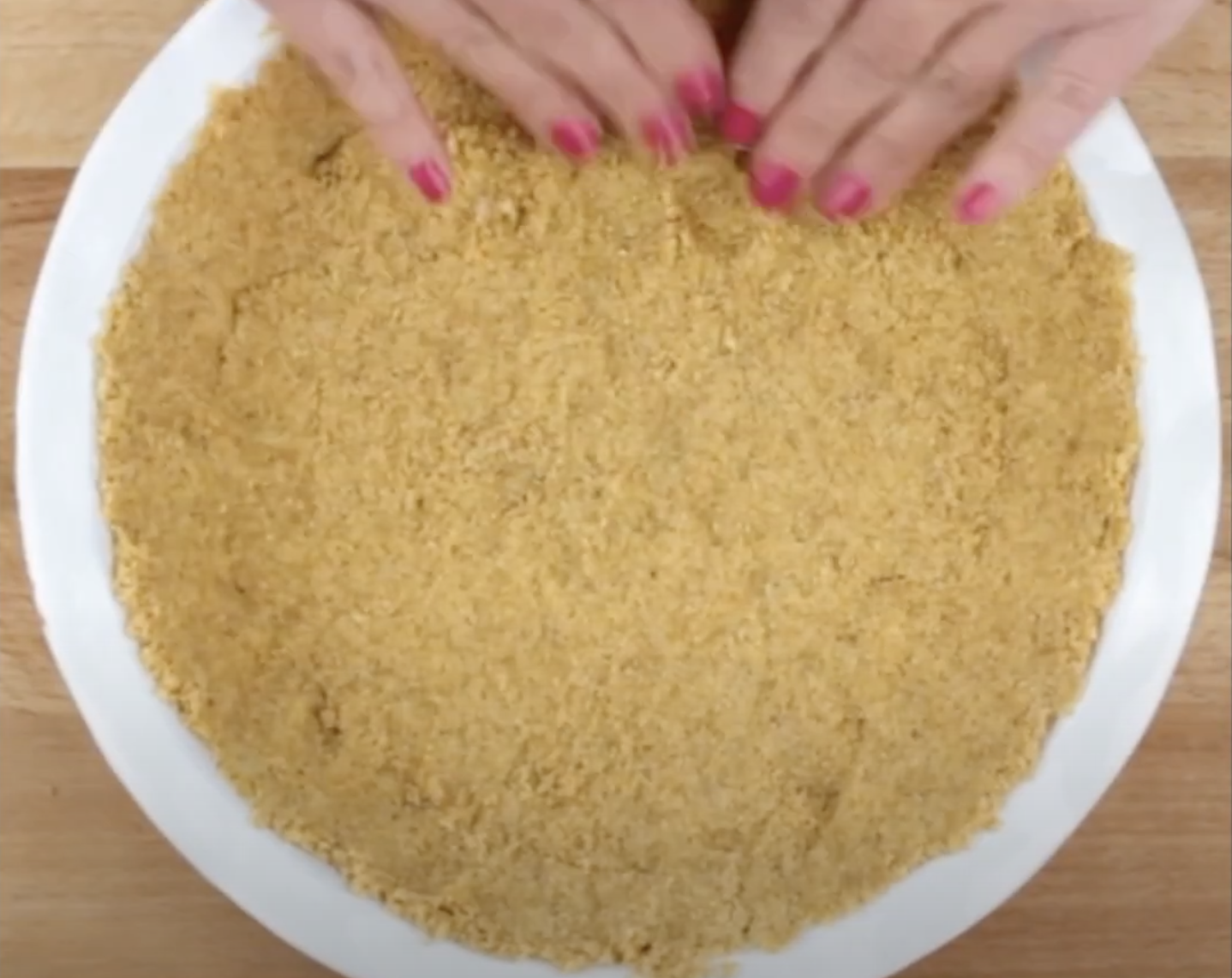 Crushed graham crackers mixed with butter being flattened in a pie dish making a homemade pie crust for key lime pie