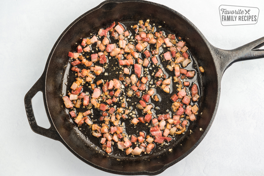 A cast iron skillet with pancetta and garlic cooking inside