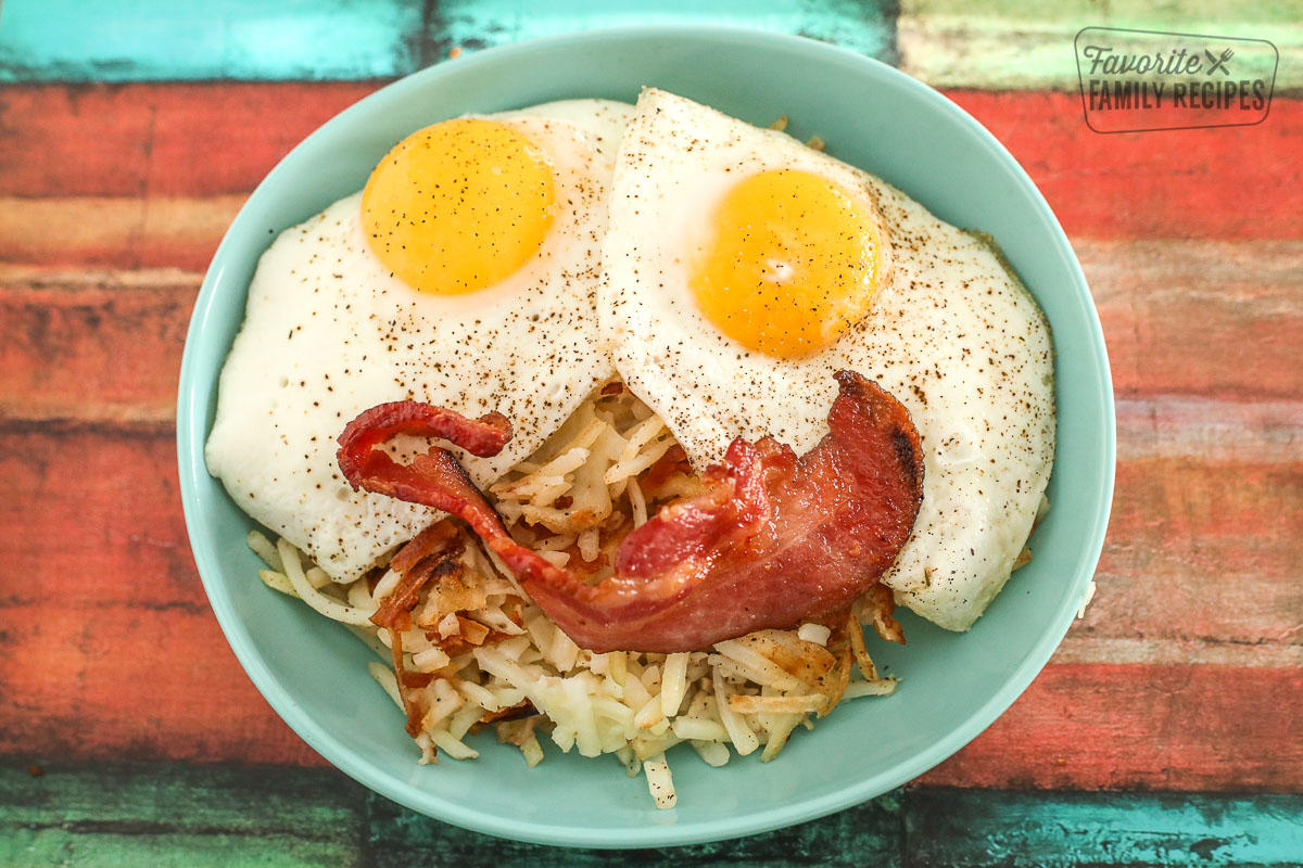 Hashbrowns, 2 eggs, and bacon in a bowl making a smiley face