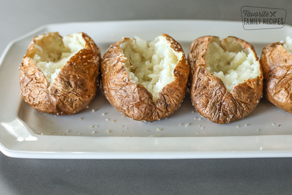 Row of baked potatoes that have been opened and mashed inside.