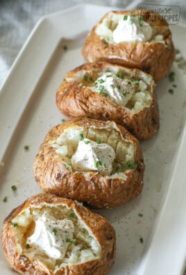 Four baked potatoes on a platter with sour cream and chives.